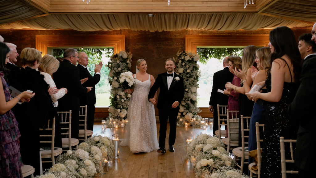 A bride and groom's exit down the aisle after getting married  with guests applauding. At Elmore Court, The Cotswolds